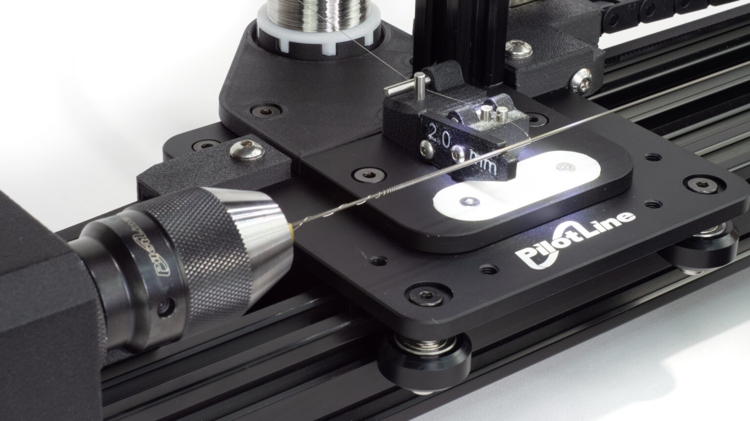 A close up of a coil winder showing a thin stainless wire being wound over a mandrel under tension. A keyless three jaw chuck is holding the left side of the mandrel.